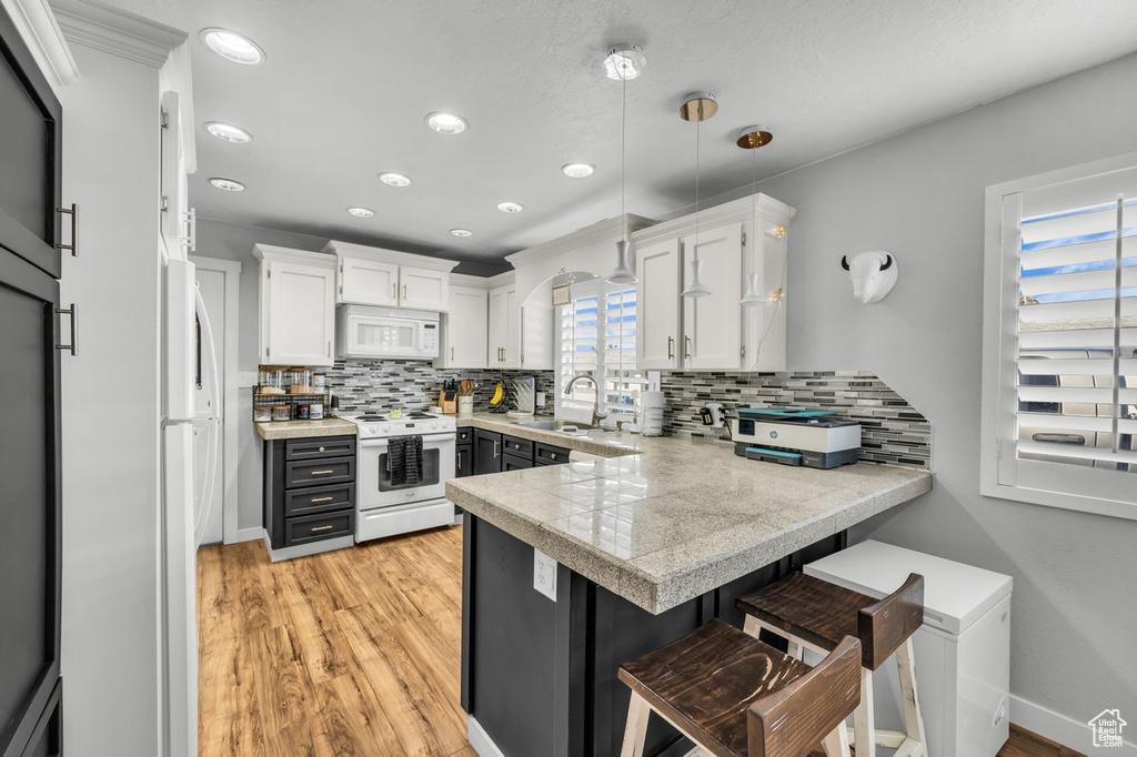 Kitchen featuring white cabinets, white appliances, kitchen peninsula, and a kitchen breakfast bar