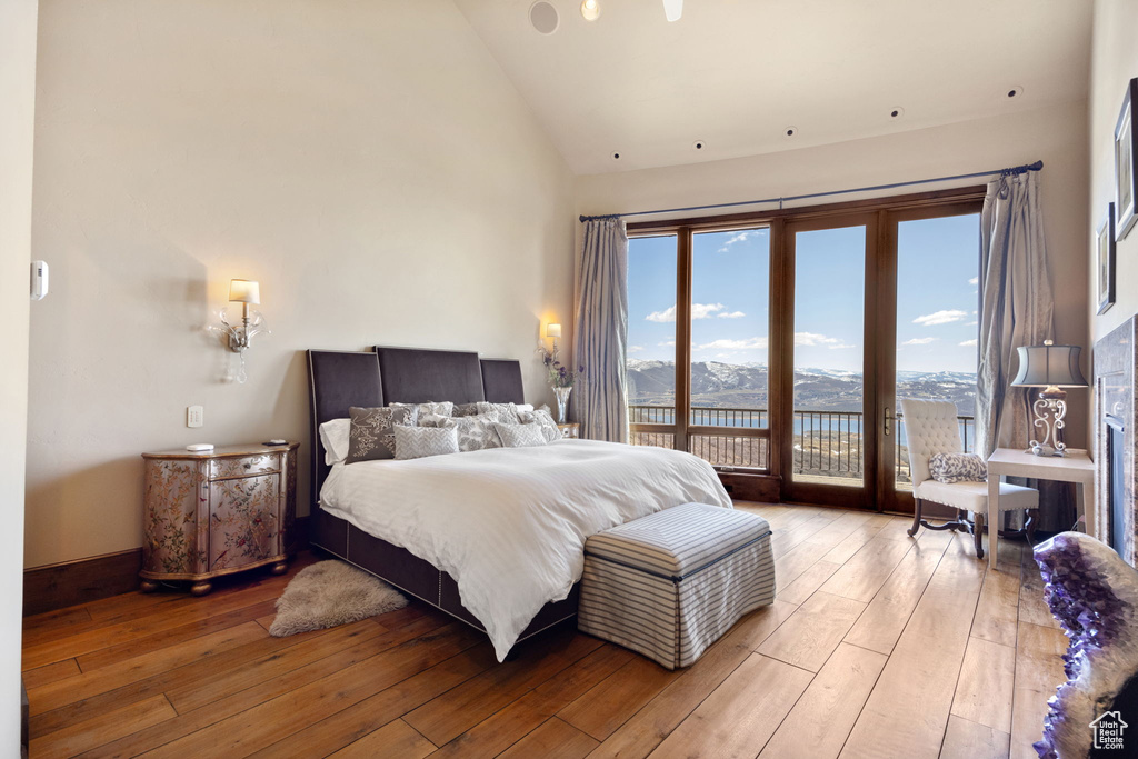 Bedroom with high vaulted ceiling, hardwood / wood-style floors, access to exterior, and a water view