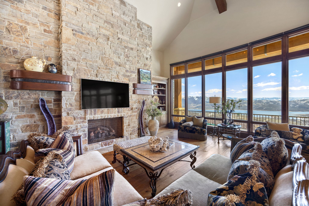 Living room featuring a water view, high vaulted ceiling, hardwood / wood-style flooring, and a stone fireplace