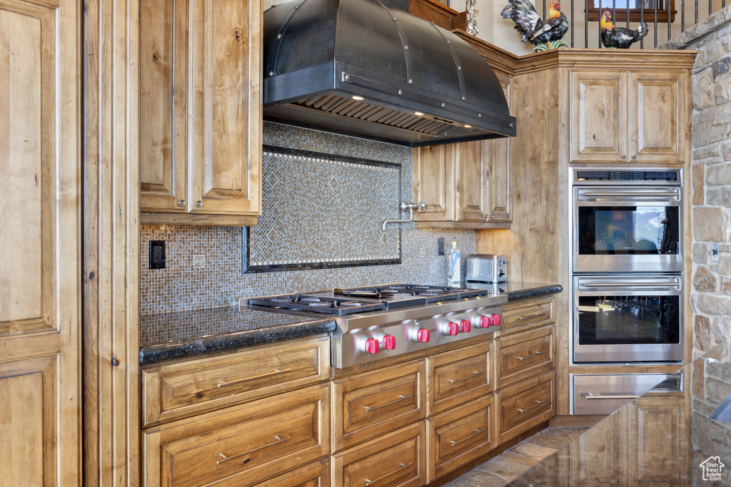 Kitchen with dark stone countertops, custom range hood, tasteful backsplash, and stainless steel appliances