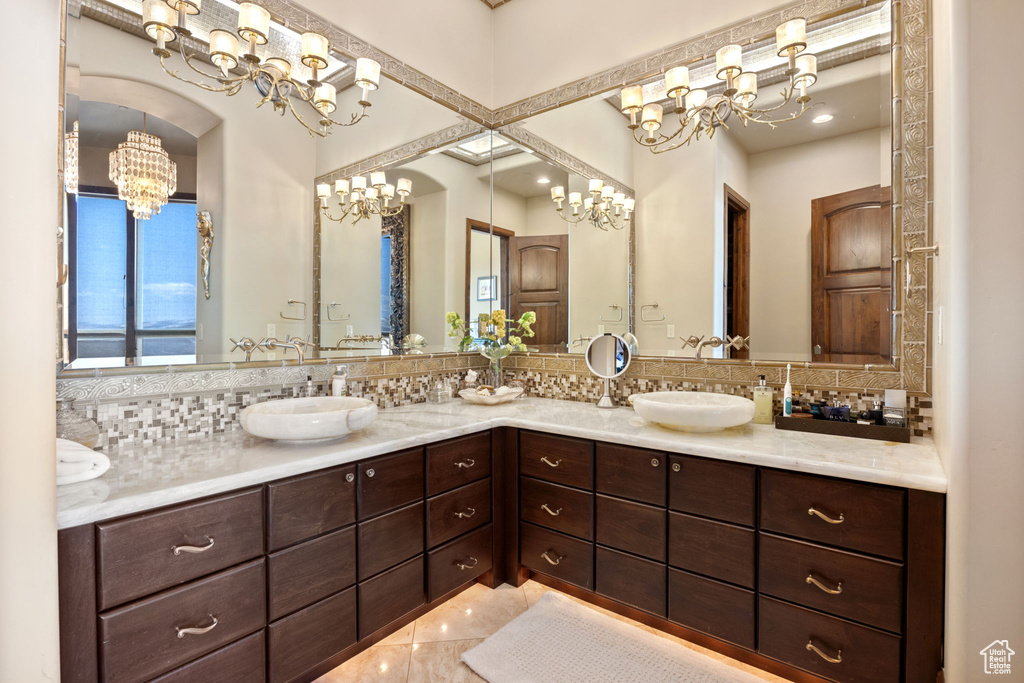 Bathroom with backsplash, an inviting chandelier, double vanity, and tile floors