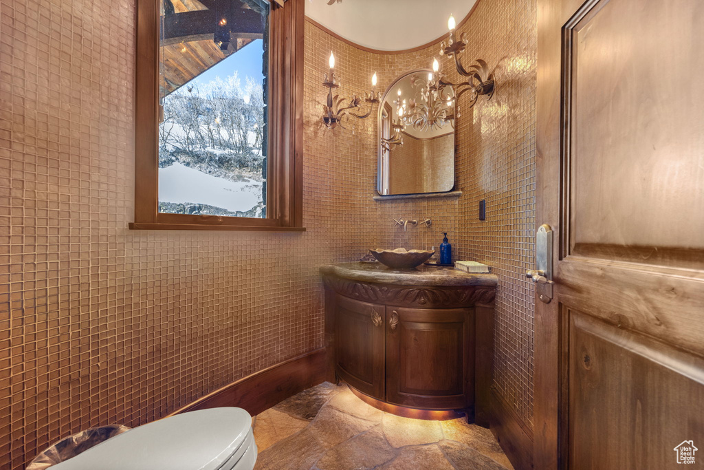 Bathroom featuring tile floors, vanity, tile walls, an inviting chandelier, and toilet