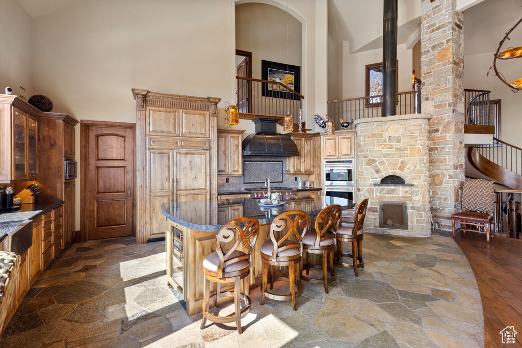Kitchen with wall chimney exhaust hood, high vaulted ceiling, double oven, hardwood / wood-style floors, and a kitchen island