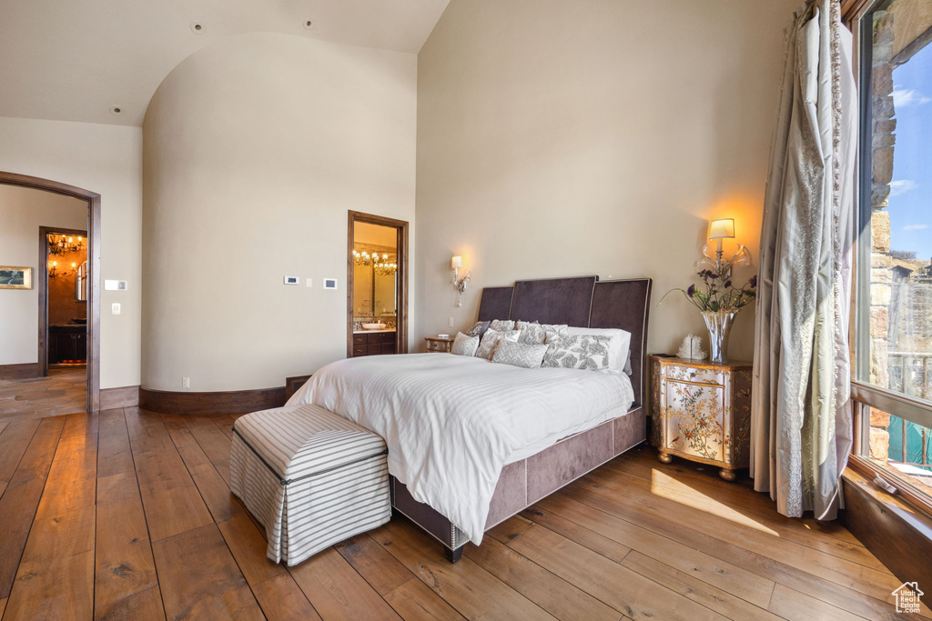 Bedroom featuring high vaulted ceiling, hardwood / wood-style flooring, and connected bathroom