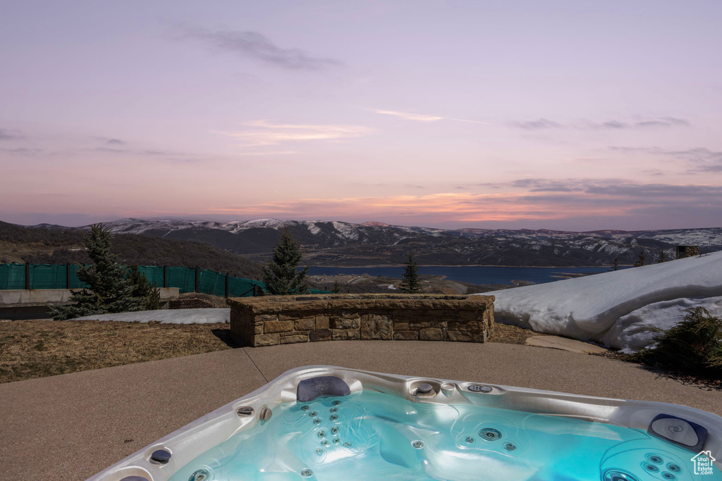 Pool at dusk with a mountain view and an outdoor hot tub