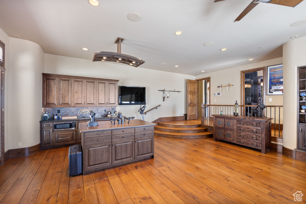Kitchen with ceiling fan, a center island, backsplash, hardwood / wood-style floors, and stainless steel microwave