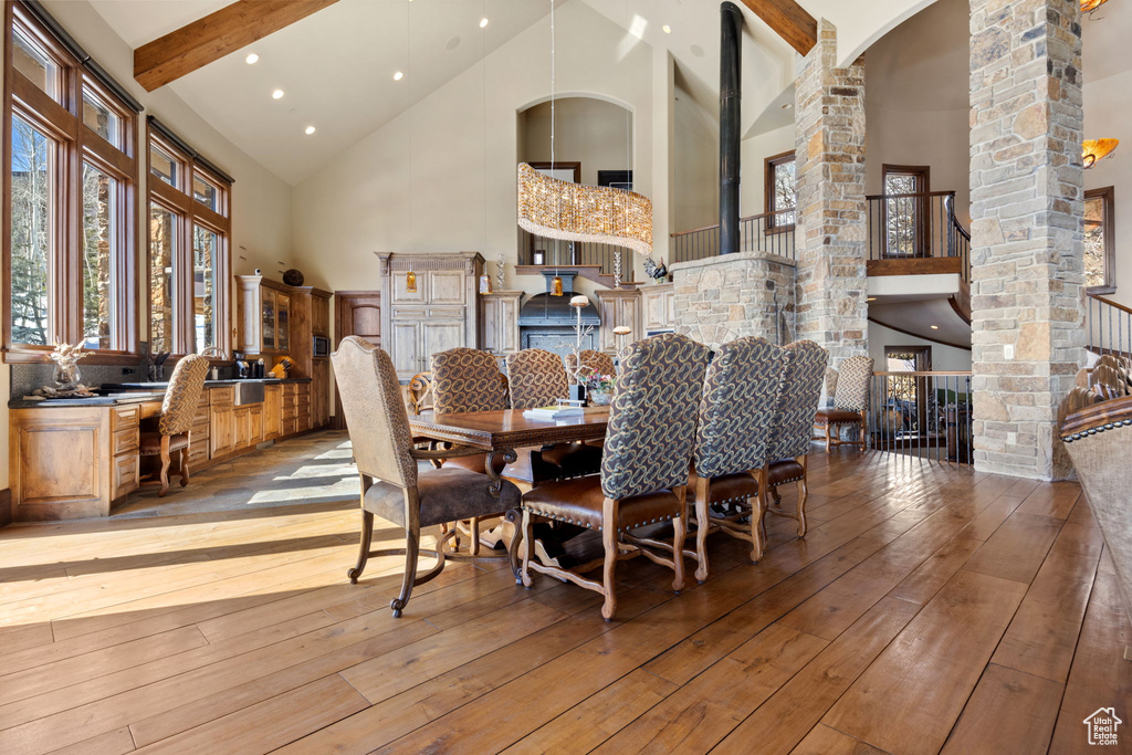 Dining area with high vaulted ceiling, light hardwood / wood-style floors, beam ceiling, and decorative columns