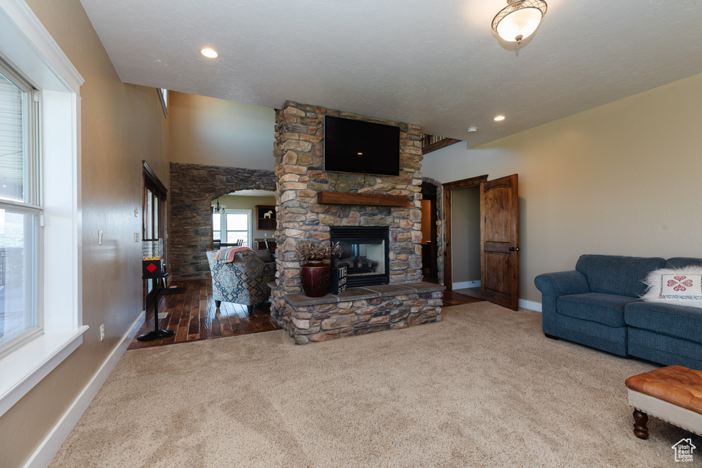 Living room with dark hardwood / wood-style flooring, lofted ceiling, and a stone fireplace