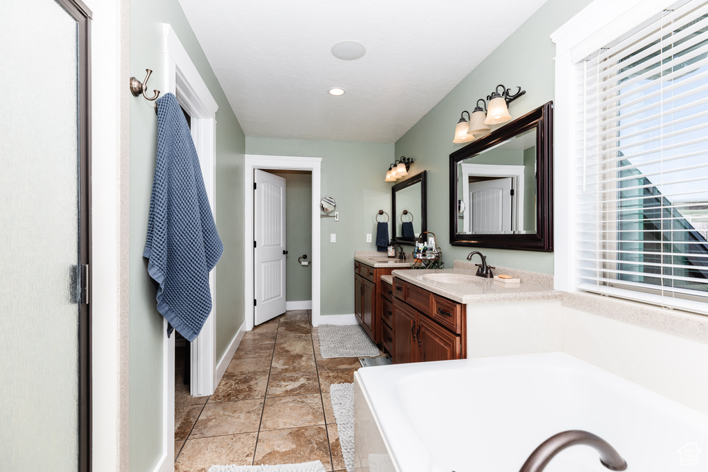 Bathroom featuring a tub, dual sinks, vanity with extensive cabinet space, and tile flooring