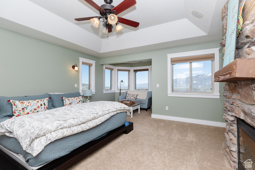 Carpeted bedroom featuring a fireplace, ceiling fan, and a tray ceiling