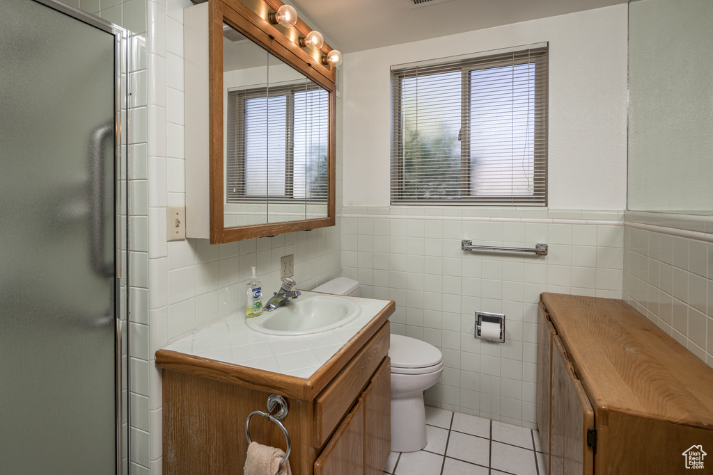 Bathroom with vanity, toilet, tile flooring, and tile walls