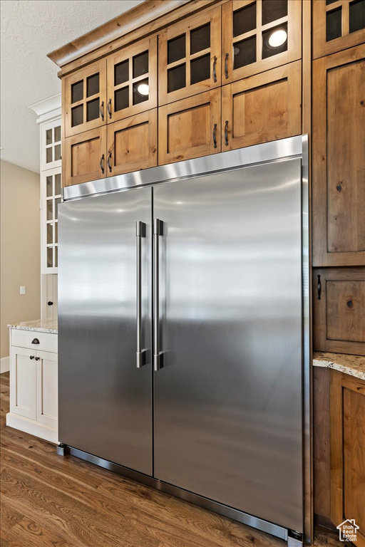 Kitchen with stainless steel built in fridge, light stone countertops, and dark wood-type flooring