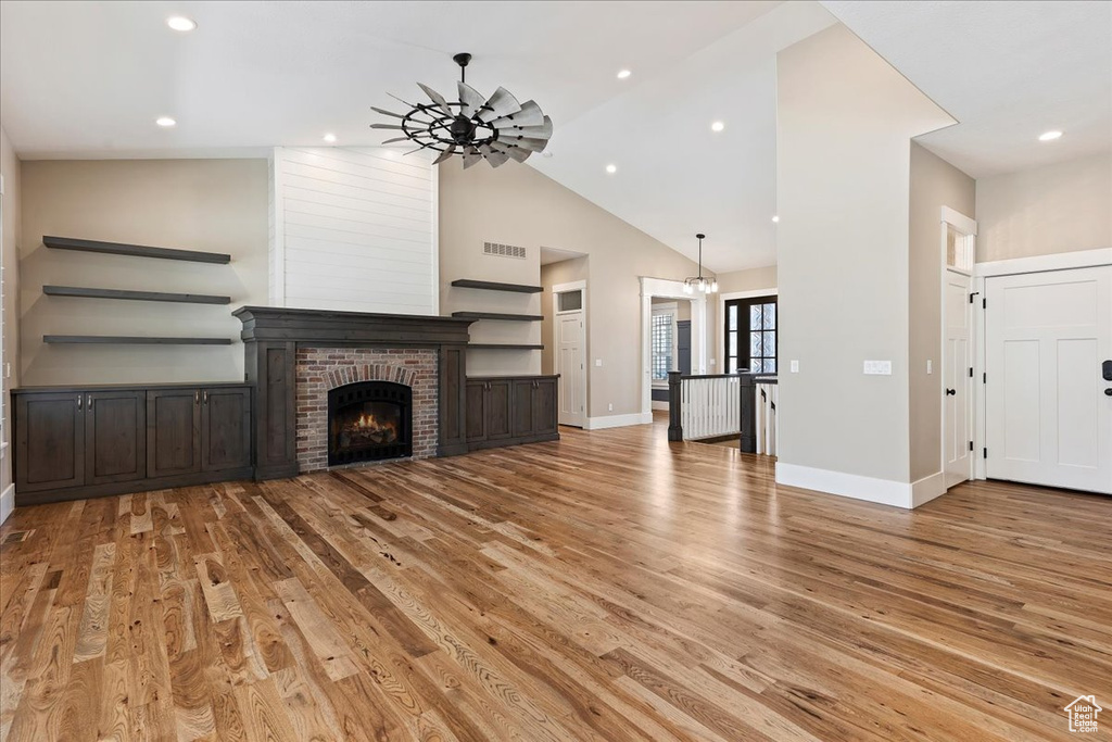Unfurnished living room with high vaulted ceiling, light hardwood / wood-style floors, ceiling fan, and a fireplace