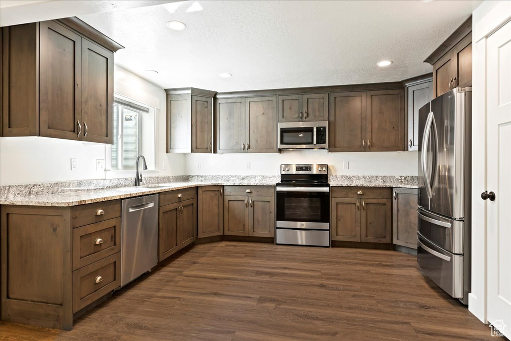 Kitchen featuring appliances with stainless steel finishes, sink, dark brown cabinets, dark hardwood / wood-style flooring, and light stone countertops