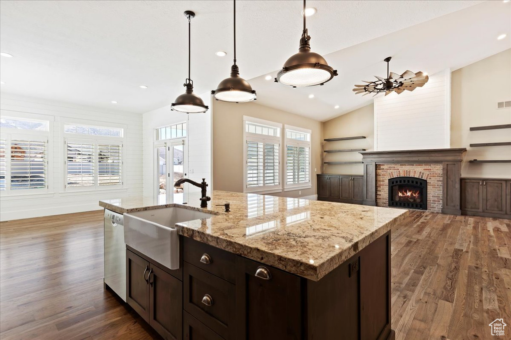 Kitchen featuring hanging light fixtures, dark wood-type flooring, a brick fireplace, and an island with sink