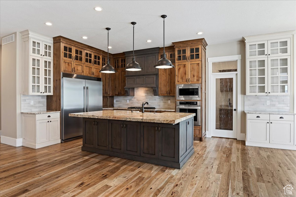 Kitchen featuring built in appliances, light hardwood / wood-style flooring, an island with sink, and white cabinetry
