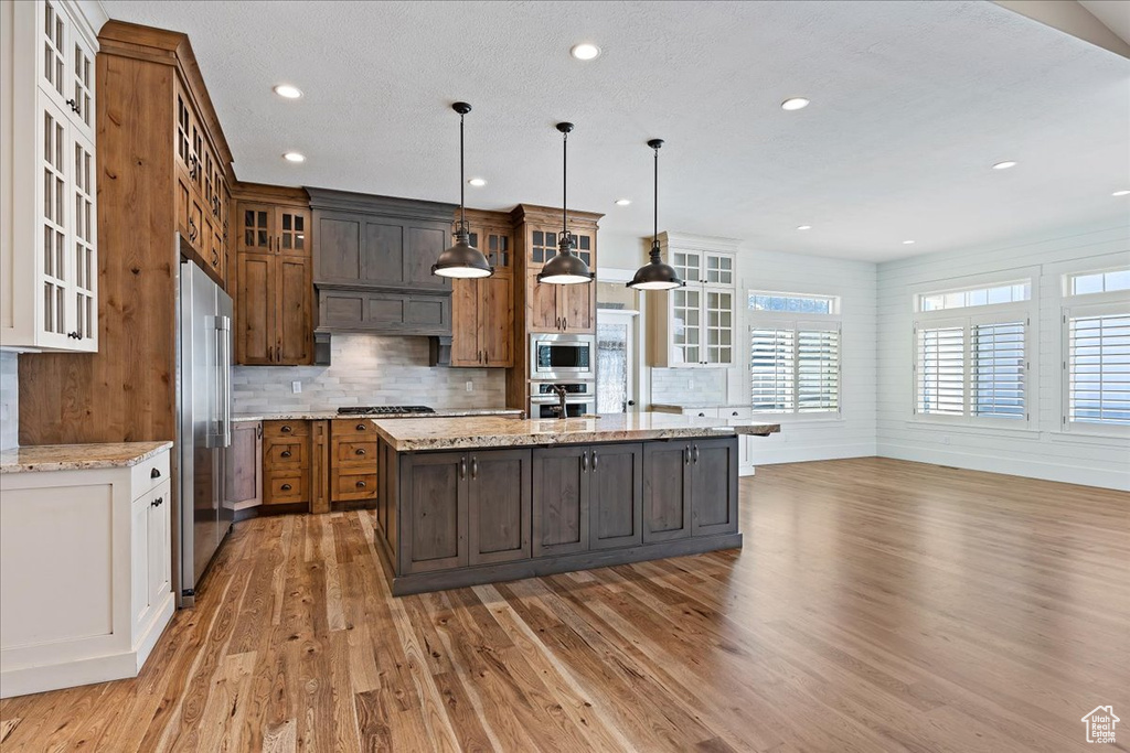 Kitchen with appliances with stainless steel finishes, hardwood / wood-style floors, an island with sink, and decorative light fixtures
