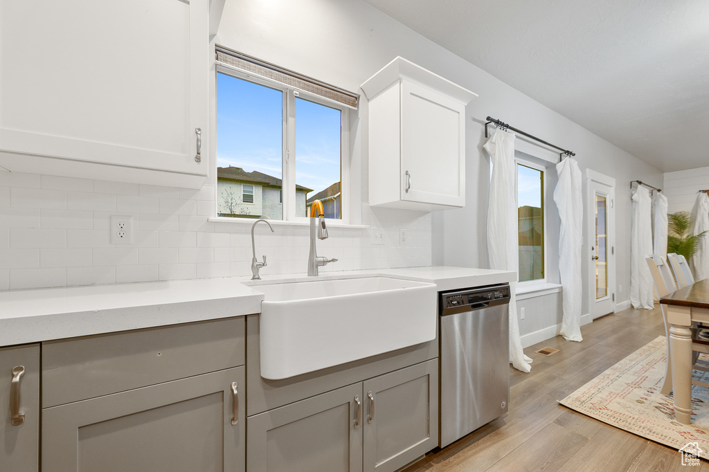 Kitchen featuring backsplash, light hardwood / wood-style flooring, white cabinetry, sink, and stainless steel dishwasher