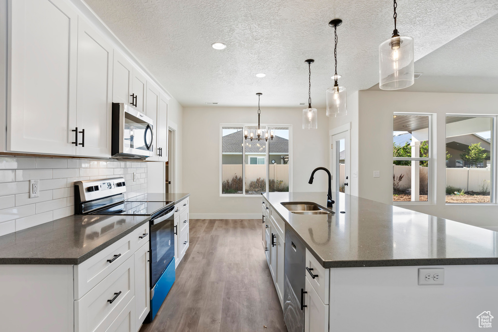 Kitchen with pendant lighting, white cabinets, stainless steel appliances, light hardwood / wood-style flooring, and a kitchen island with sink