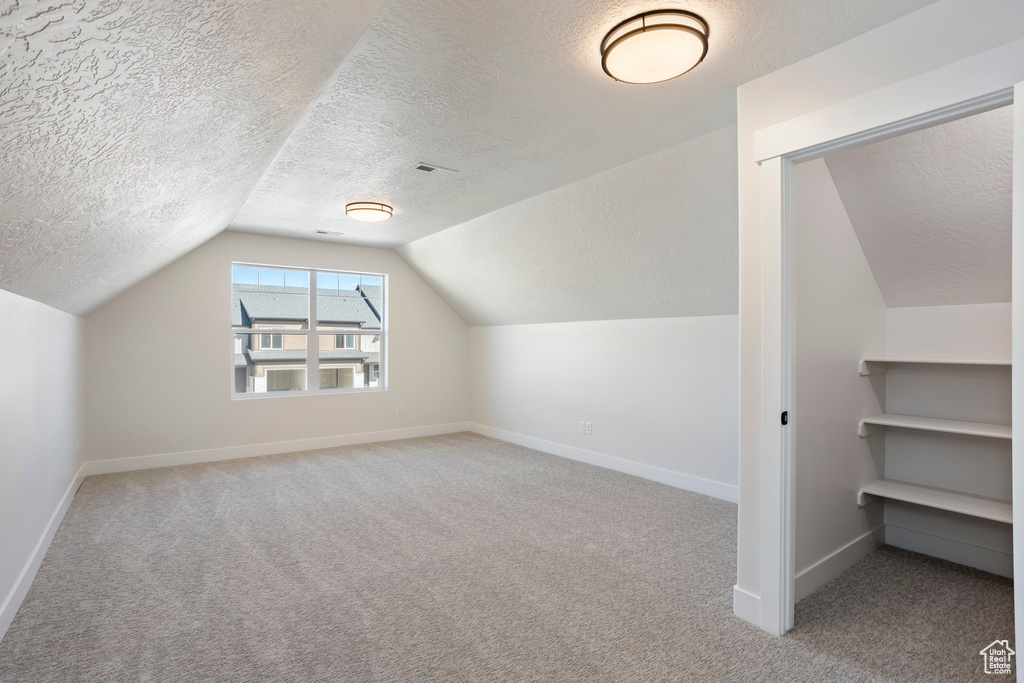 Bonus room featuring light colored carpet, vaulted ceiling, and a textured ceiling