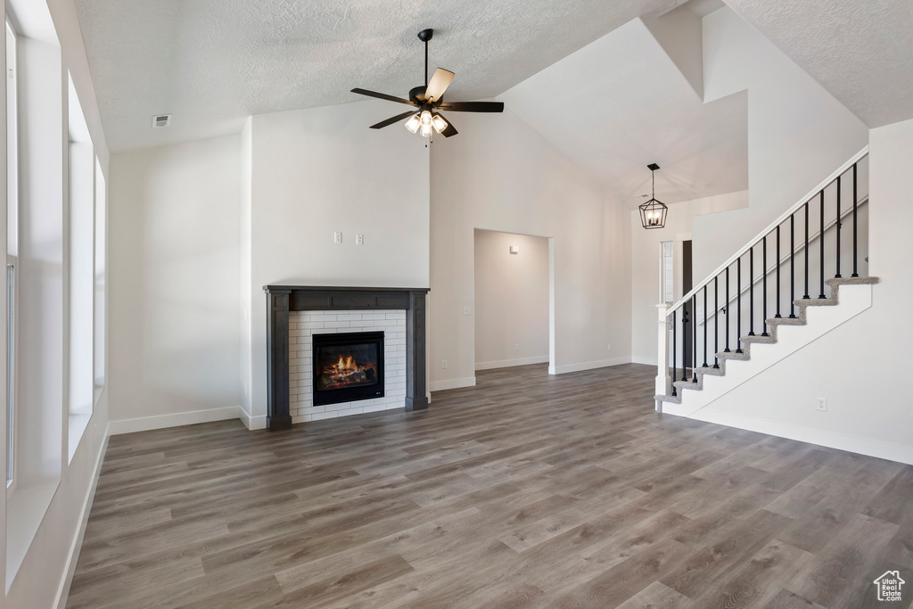 Unfurnished living room with a fireplace, a textured ceiling, high vaulted ceiling, ceiling fan with notable chandelier, and hardwood / wood-style floors