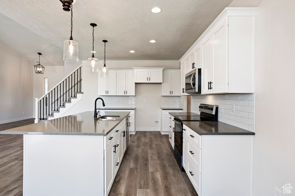 Kitchen with dark hardwood / wood-style flooring, stainless steel appliances, white cabinetry, and decorative light fixtures