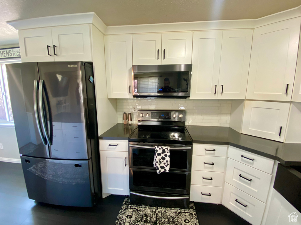 Kitchen with backsplash, appliances with stainless steel finishes, dark wood-type flooring, and white cabinets