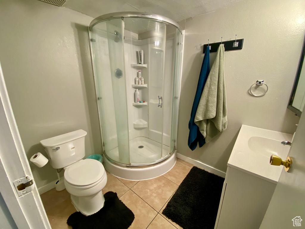 Bathroom with a shower with shower door, toilet, tile floors, and vanity