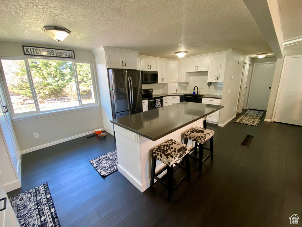 Kitchen featuring appliances with stainless steel finishes, a kitchen island, white cabinetry, dark hardwood / wood-style flooring, and a breakfast bar