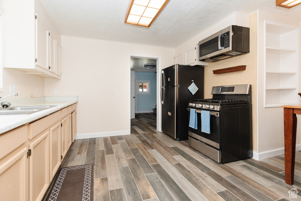 Kitchen with appliances with stainless steel finishes, light hardwood / wood-style floors, white cabinetry, and sink