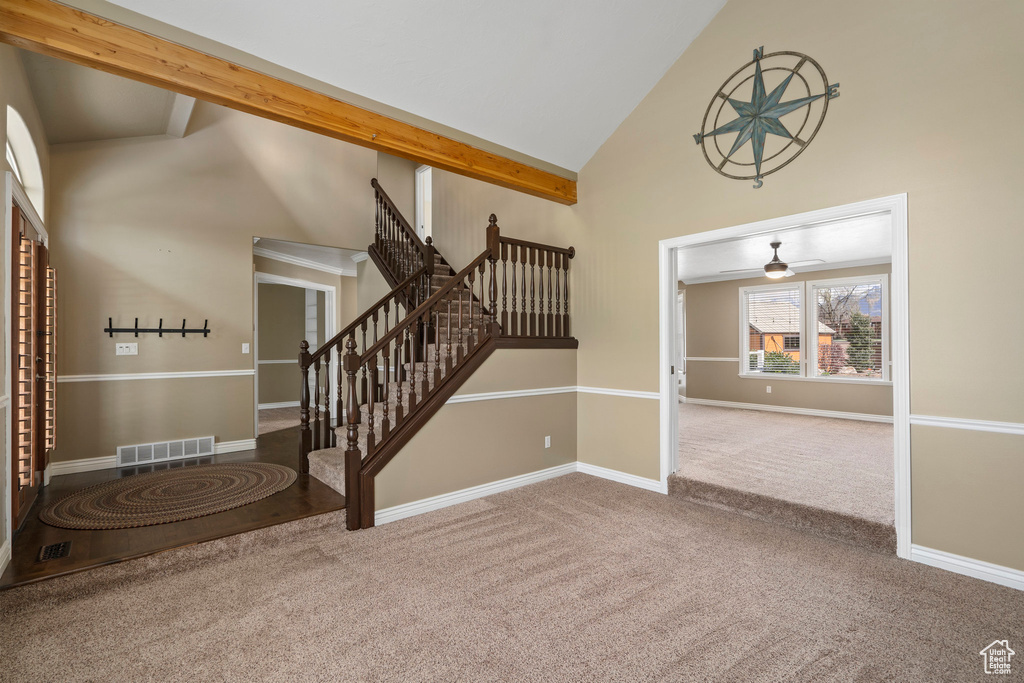 Foyer entrance featuring light colored carpet, beamed ceiling, ceiling fan, and high vaulted ceiling