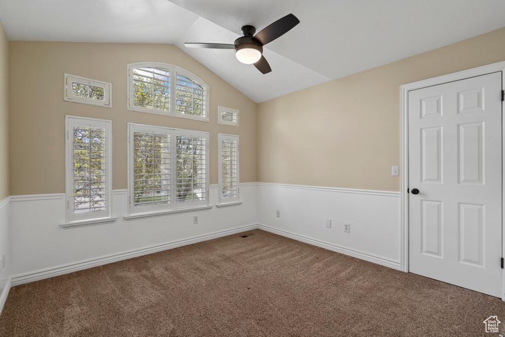 Unfurnished room featuring lofted ceiling, ceiling fan, and dark colored carpet