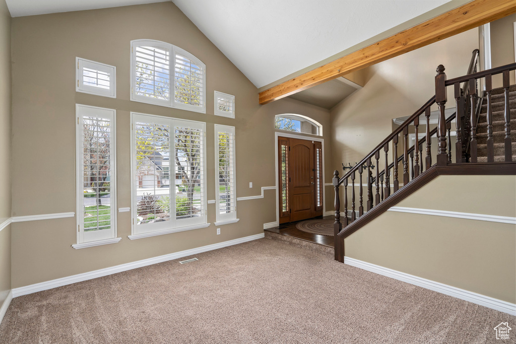 Carpeted entryway with high vaulted ceiling, beam ceiling, and a wealth of natural light