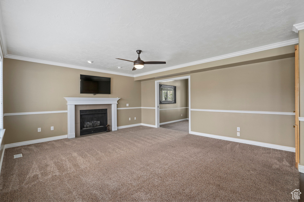 Unfurnished living room with ceiling fan, crown molding, a tile fireplace, and dark colored carpet
