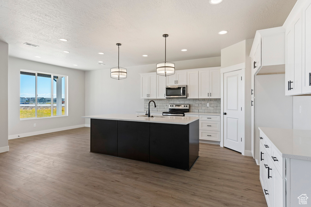 Kitchen with appliances with stainless steel finishes, backsplash, white cabinetry, dark hardwood / wood-style flooring, and a center island with sink