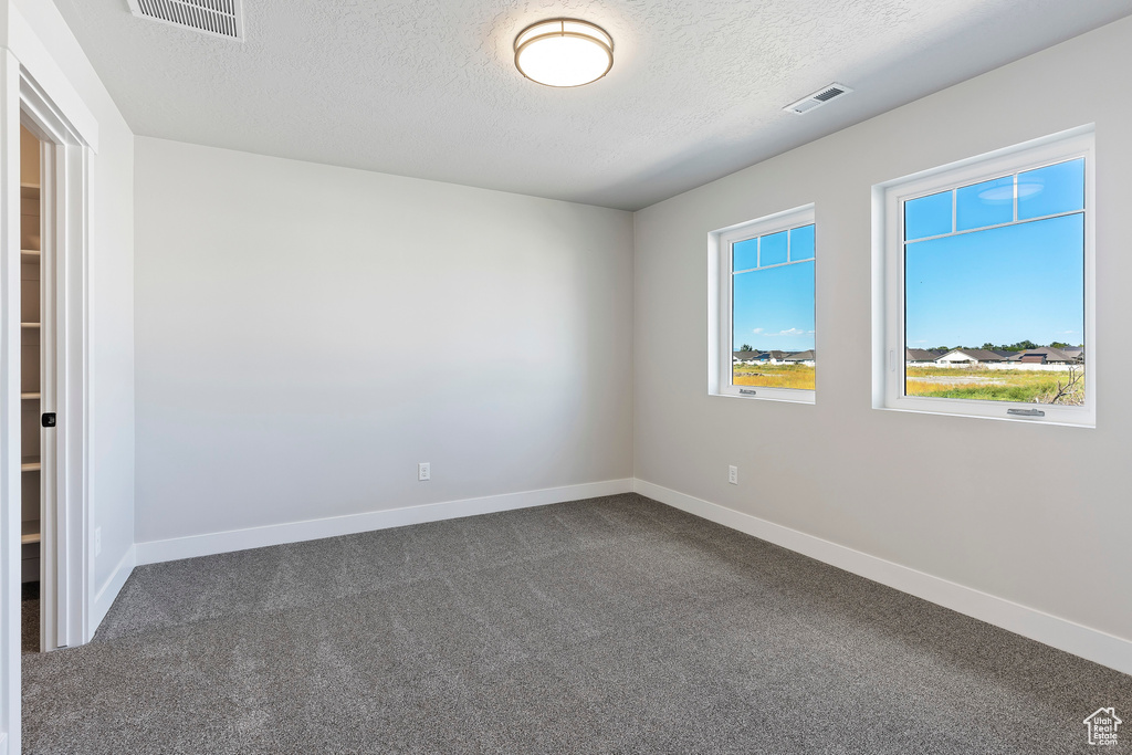 Empty room with dark colored carpet and a textured ceiling