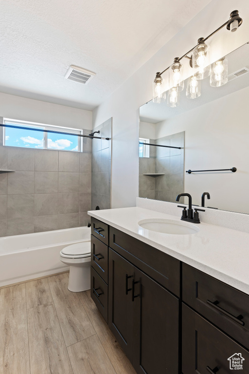 Full bathroom featuring wood-type flooring, toilet, oversized vanity, and tiled shower / bath combo