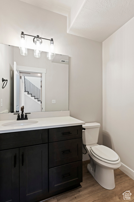 Bathroom featuring a textured ceiling, toilet, vanity, and hardwood / wood-style floors