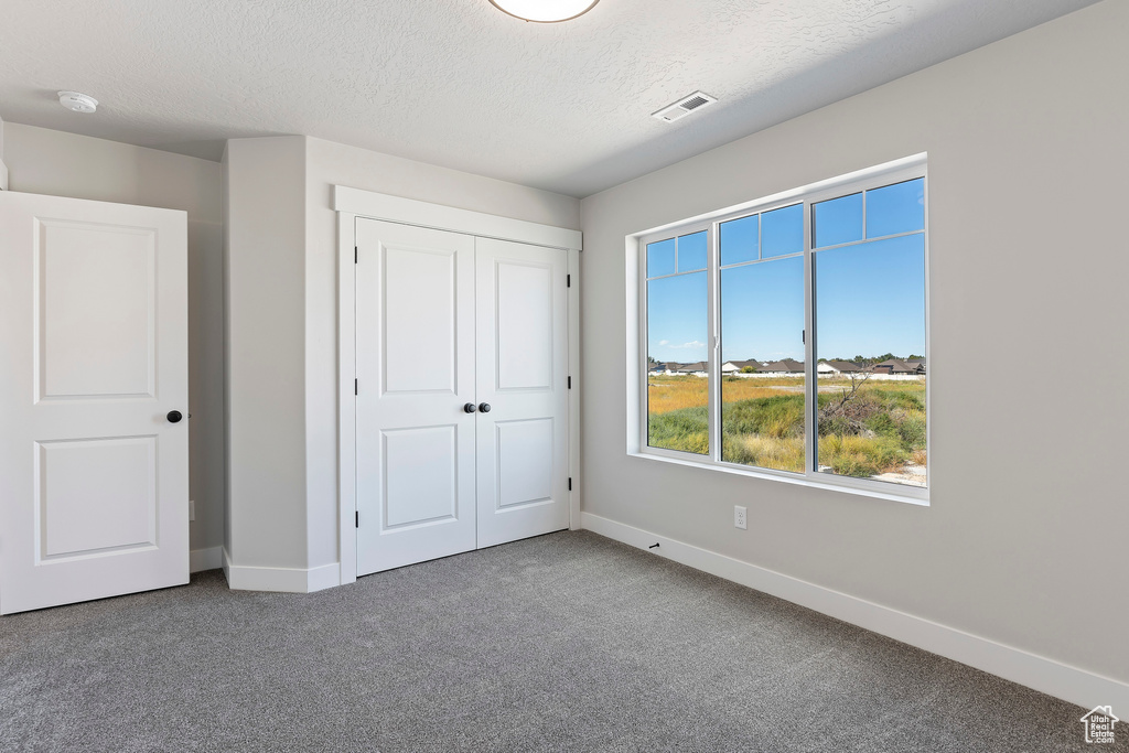 Unfurnished bedroom featuring dark colored carpet, a closet, and a textured ceiling