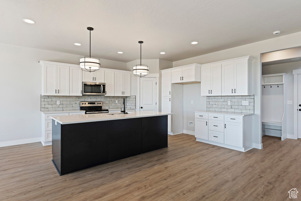 Kitchen with white cabinets, light hardwood / wood-style flooring, pendant lighting, and stainless steel appliances