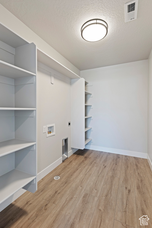 Clothes washing area featuring hookup for an electric dryer, light wood-type flooring, and a textured ceiling