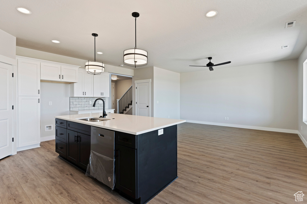 Kitchen featuring hanging light fixtures, light wood-type flooring, white cabinetry, backsplash, and sink