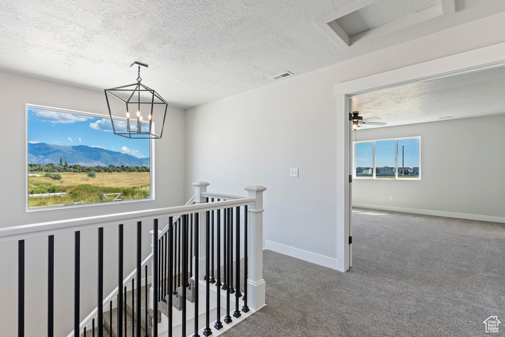 Corridor featuring dark colored carpet, a textured ceiling, a mountain view, and an inviting chandelier