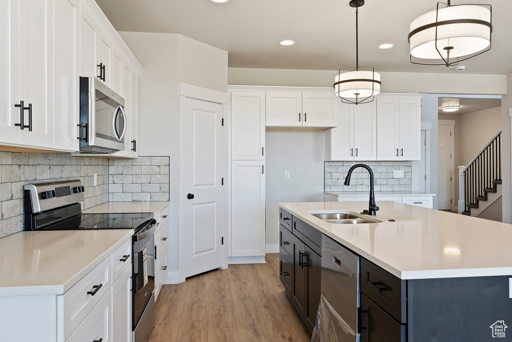 Kitchen with decorative light fixtures, light wood-type flooring, white cabinets, and stainless steel appliances