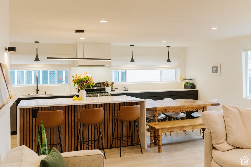 Kitchen featuring stove, decorative light fixtures, light hardwood / wood-style flooring, sink, and range hood