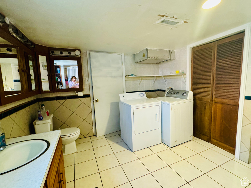 Laundry room featuring tile walls, sink, light tile floors, and washing machine and clothes dryer