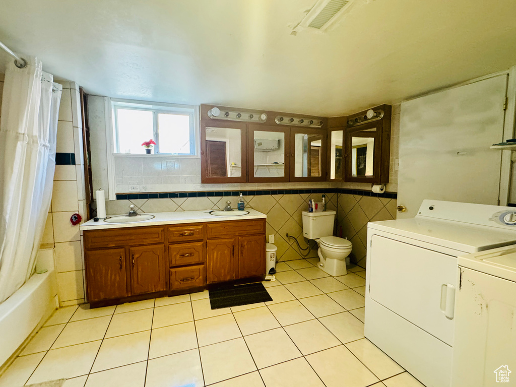 Laundry area with light tile flooring, tile walls, sink, and washer and dryer