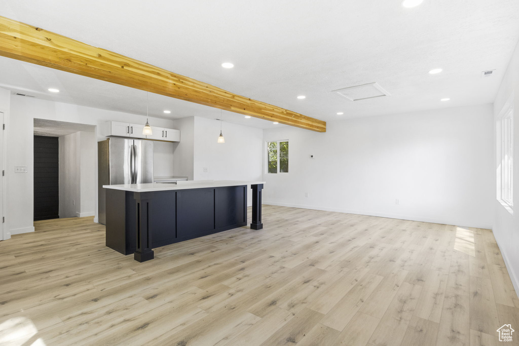 Kitchen featuring a kitchen island, white cabinets, beamed ceiling, pendant lighting, and light wood-type flooring