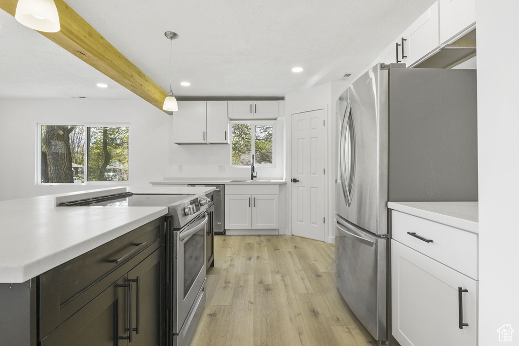 Kitchen featuring white cabinets, light hardwood / wood-style floors, appliances with stainless steel finishes, and pendant lighting