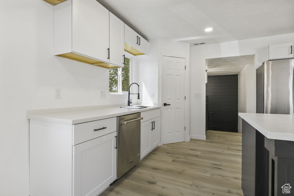Kitchen with stainless steel appliances, white cabinetry, sink, and light wood-type flooring